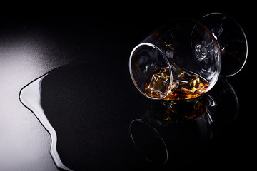 Snifter glass with cognac (brandy snifter, brandy bowl, cognac glass, or balloon) lying on a black background with reflection.