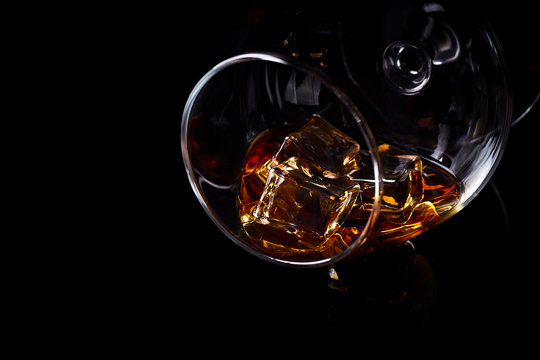 Snifter glass with cognac (brandy snifter, brandy bowl, cognac glass, or balloon) lying on a black background with reflection.