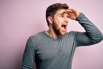 Young handsome blond man with beard and blue eyes wearing casual sweater very happy and smiling looking far away with hand over head. Searching concept.