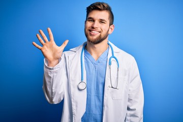 Young blond doctor man with beard and blue eyes wearing white coat and stethoscope showing and...