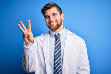 Young blond therapist man with beard and blue eyes wearing coat and tie over background showing and pointing up with fingers number three while smiling confident and happy.