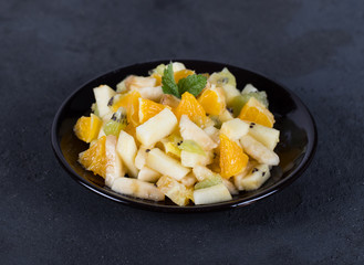 Fruit vitamin salad of kiwi, banana, Apple and orange on a plate on a dark gray background 