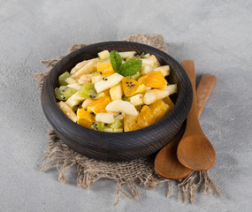 Fruit vitamin salad of kiwi, banana, Apple and orange in a wooden bowl on a light gray background in rustic style
