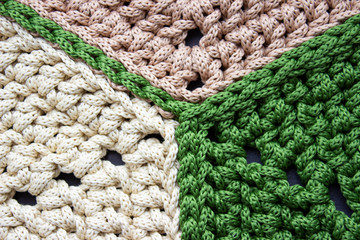 Knitting from a cord. Crocheted carpet of hexagons. Beige and green. Knitting texture.