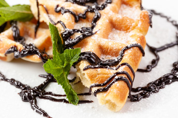 Belgian waffles in powdered sugar with chocolate syrup and mint