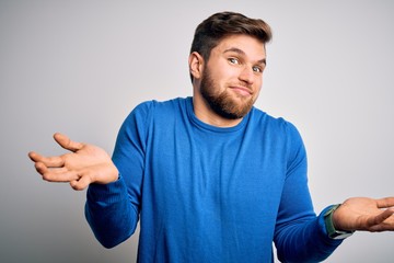 Young handsome blond man with beard and blue eyes wearing casual sweater clueless and confused expression with arms and hands raised. Doubt concept.