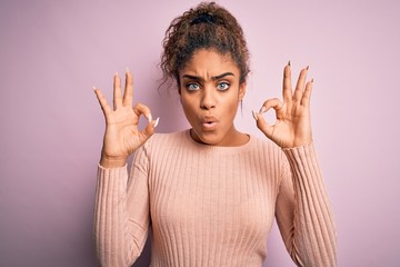 Young beautiful african american girl wearing casual sweater standing over pink background looking...