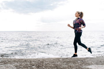 Jogging outdoors. Cardio workout. Young attractive athletic girl in sportswear is jogging outdoor near the sea