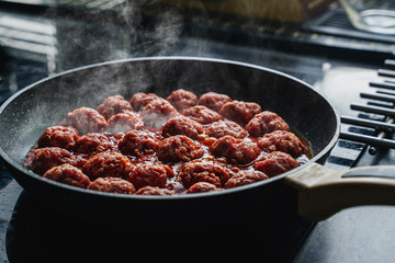 meatballs are cooked in a black frying pan with a haze 