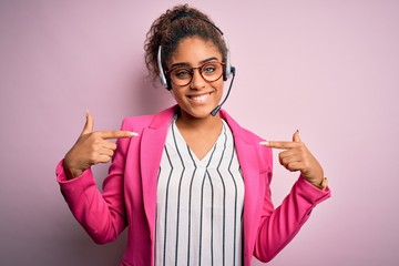 Young african american call center agent girl wearing glasses working using headset looking confident with smile on face, pointing oneself with fingers proud and happy.