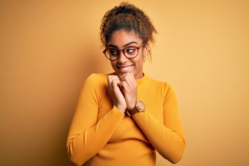 Young beautiful african american girl wearing sweater and glasses over yellow background laughing...