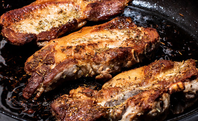 Obraz na płótnie Canvas Fried juicy meat is covered with a crispy crust. In a cast-iron pan with salt and rosemary. Top and side view, on a light background