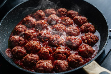 meatballs are cooked in a black frying pan with a haze 