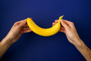 hands holding a bright yellow banana on a blue background