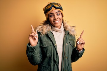 Young african american afro skier girl wearing snow sportswear and ski goggles smiling confident pointing with fingers to different directions. Copy space for advertisement