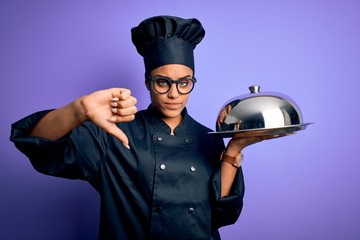 Young african american cooker girl wearing uniform and hat holding tray with dome with angry face, negative sign showing dislike with thumbs down, rejection concept