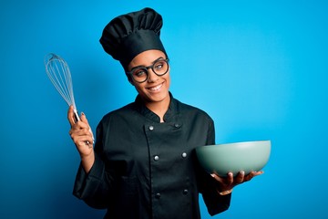 Young african american chef girl wearing cooker uniform and hat using whisk and bowl with a happy...