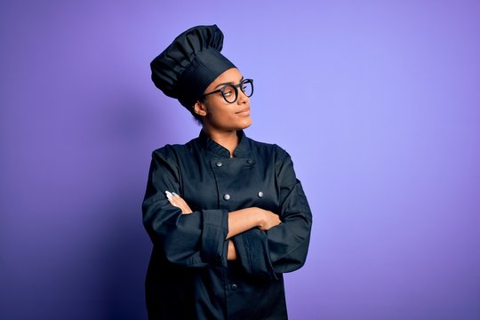 Young african american chef girl wearing cooker uniform and hat over purple background looking to the side with arms crossed convinced and confident