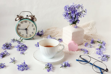 Obraz na płótnie Canvas The concept of good morning and good mood : a Cup of tea, an alarm clock and a bouquet of blue flowers on the table with a pink heart, side view