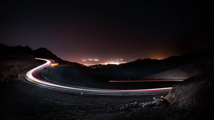 highway long exposure vehicle light trails curvy highway between mountains at starry night 