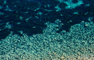 Seabed with pebbles and black spots  in a clear water.Top view.