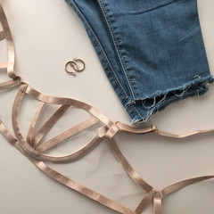 Beautiful beige bra top view. Fashionable bra concept. Stretch mesh underwear. Gold earrings trend rings. Light fringed jeans. Accessories for underwear. 
Stylish, modern look 2020