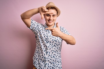 Handsome redhead man on vacation wearing casual shirt and hat over isolated pink background smiling making frame with hands and fingers with happy face. Creativity and photography concept.