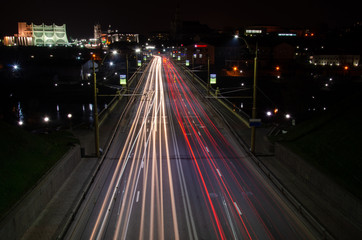Fototapeta na wymiar Night city. The light trails on the street. Slow shutter speed photo. A long bridge across the river leads to the big city. A busy expressway in the town center.