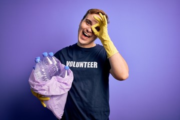 Young handsome redhead volunteer man doing volunteering holding bag with plastic bottles smiling...