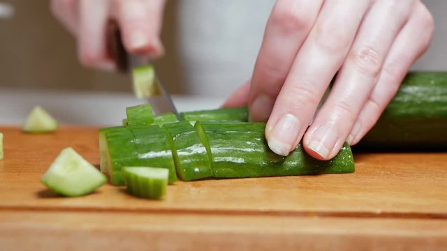 Closeup of female hands cutting a cucumber on wooden board