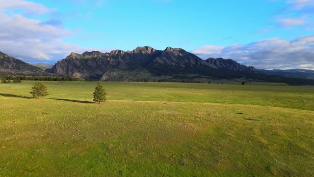 fly over green fields towards flatiron mountains during sunrise in colorado