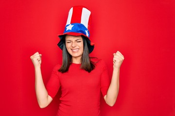 Young beautiful brunette woman wearing united states hat celebrating independence day very happy and excited doing winner gesture with arms raised, smiling and screaming for success. Celebration