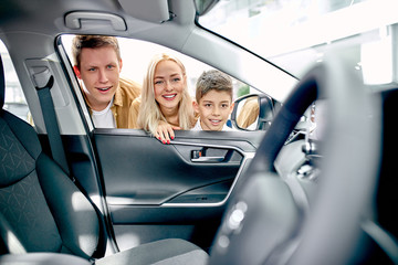 positive young happy family inspecting car from inside, look at wheel and they are surprised with design of auto