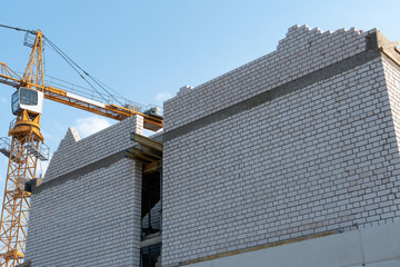 Orange tower crane against a clear blue sky. Construction of a new brick building. Modern construction site. Housing on credit, mortgages, sale of real estate.