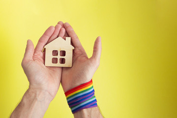 male hands with rainbow gay pride LGBT ribbon wristband holding small wooden house