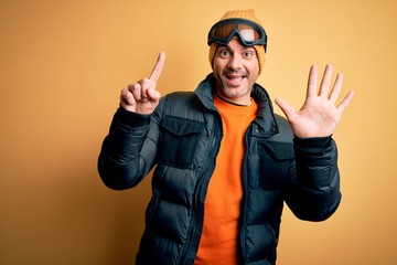 Young handsome skier man skiing wearing snow sportswear using ski goggles showing and pointing up with fingers number six while smiling confident and happy.