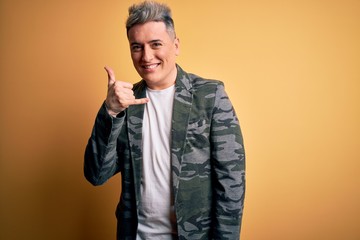 Young handsome modern man wearing business jacket standing over yellow isolated background smiling doing phone gesture with hand and fingers like talking on the telephone. Communicating concepts.