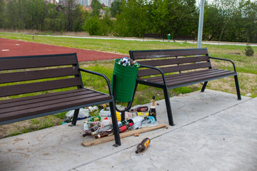Moscow, Russia - 05/20/2020 - Two benches and lot of trash near the full trash bin. Dirty streets...