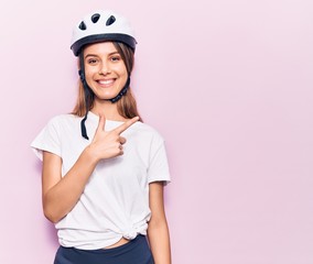 Young beautiful girl wearing bike helmet smiling cheerful pointing with hand and finger up to the side