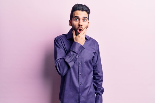 Young handsome man with beard wearing casual shirt looking fascinated with disbelief, surprise and amazed expression with hands on chin