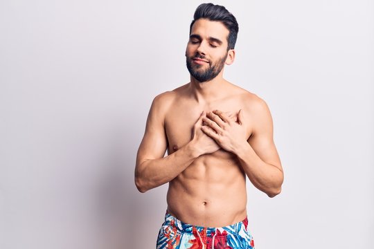 Young handsome man with beard shirtless wearing swimwear smiling with hands on chest, eyes closed with grateful gesture on face. health concept.