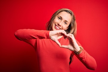 Young beautiful blonde woman wearing casual t-shirt standing over isolated red background smiling...