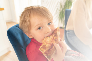 Cute blonde boy eating slice of pizza.