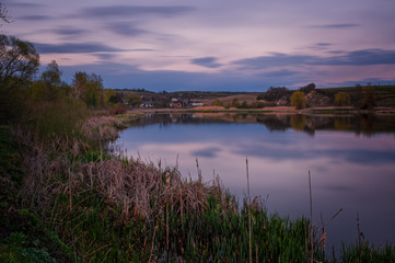 Amazing sunset view of scenic lake near medieval castle on the bank with reflection in the water and reeds on foreground. Svirzh, Ukraine. April 2020