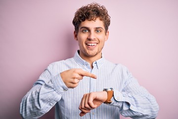 Young blond handsome man with curly hair wearing striped shirt over white background In hurry...