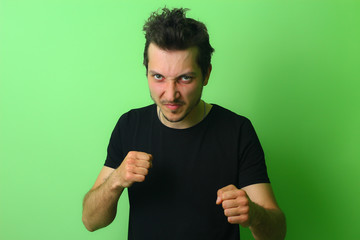 Angry young man on a light green wall background. Emotion of aggression
