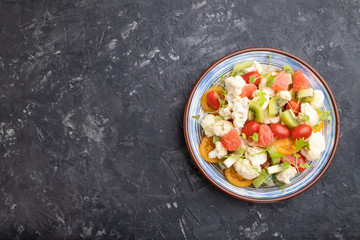 Vegetarian salad of cauliflower cabbage, kiwi, tomatoes, microgreen sprouts on black concrete background. Top view, copy space.