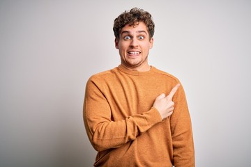 Young blond handsome man with curly hair wearing casual sweater over white background Pointing aside worried and nervous with forefinger, concerned and surprised expression