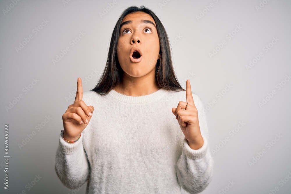 Canvas Prints Young beautiful asian woman wearing casual sweater standing over white background amazed and surprised looking up and pointing with fingers and raised arms.