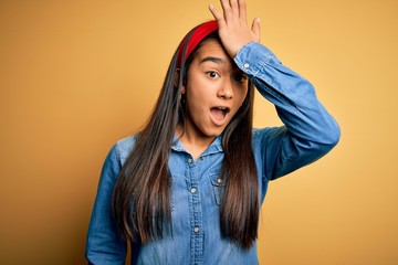 Young beautiful asian woman wearing casual denim shirt and diadem over yellow background surprised...
